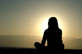 A serene morning scene with a person meditating in nature, surrounded by greenery and soft sunlight.